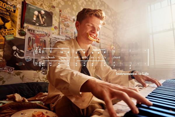 Young man oplaying piano with a piece of toast hanging out of his mouth. There is a white graphic of sheet music superimposed over the image