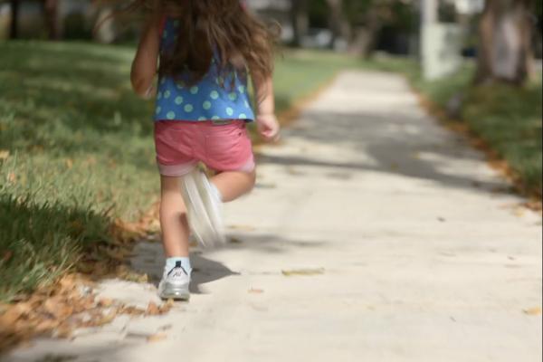 Shot from behind of a three eyar old girl in blue shirt and pink shorts running down a sidewalk