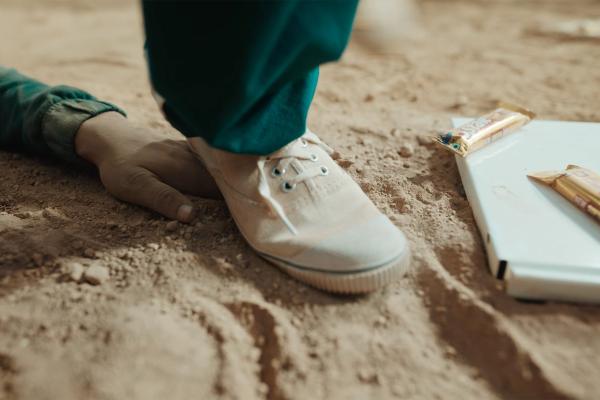 White sneaker stepping down on stand, on the ground next to the foot is a white piece of debris that has two gold Cadbury 5-Star bars on it 