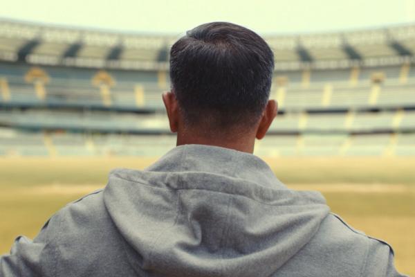 Athlete standing in an empty stadium, wearing a gray hooded sweatshirt, filmed from behind