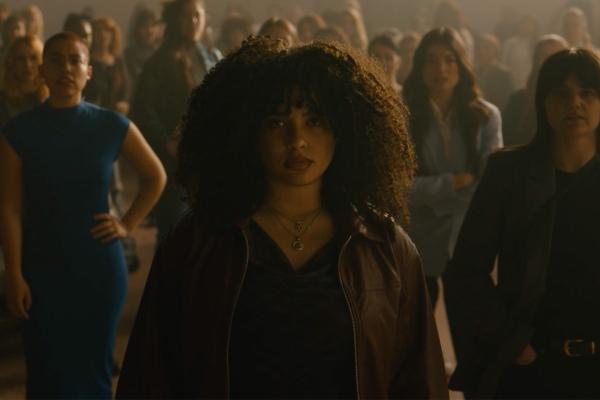 Young woman looking into the camera, in the background spread out are various other women who are all posing and looking into the camera