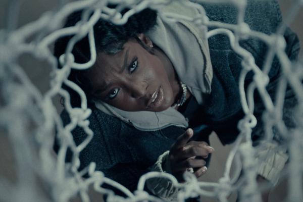 LSU athlete and hip hop artist Flau'jae Johnson looking up through the white netting of a basketball hoop, filmed from above