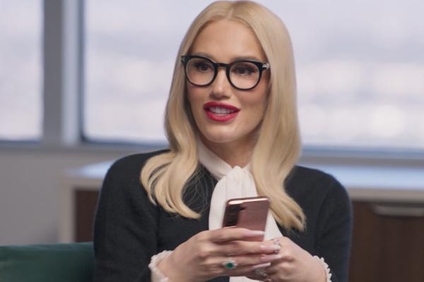 Gwen Stefani wearing business/corporate attire, holding a phone in her hands in an office setting