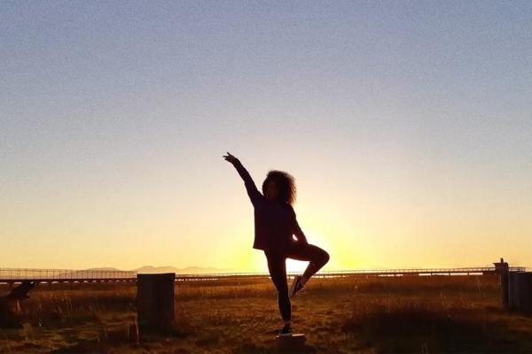 Silhoutted young person standing in a dance-like posde with one leg angled and one arm in the air 