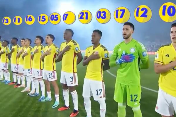 Photo of the Colombian national football team lined up, hands on heart, for the National Anthem. Above each player is a graphic of a yellow ball with a blue number inside it, akin to a lottery ball, corresponding to their jersey number