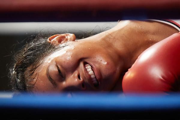 woman boxer laying face down on the canvas with a smile on her face