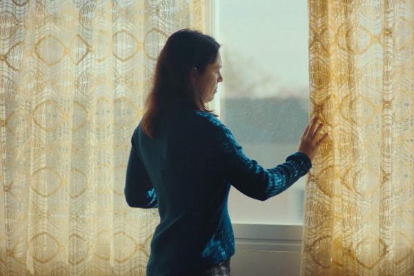 Woman at a window placing her hand on the curtain