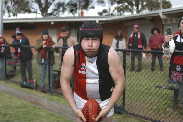 australian rules football player holding ball and looking into the camera