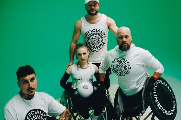 Three wheelchair rugby players pose against a vibrant green background. A man in a white tank top and cap stands behind a woman and another man, both in wheelchairs. The woman holds a white rugby ball, and all three wear white tops featuring the "OFFICIALLY UNSPONSORED" circular QR code logo.
