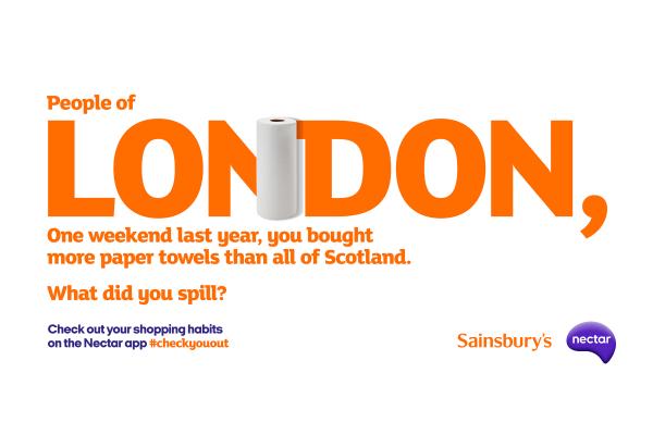 White and orange billboard describing how shoppers in London bought more kitchen roll than in Glasgow