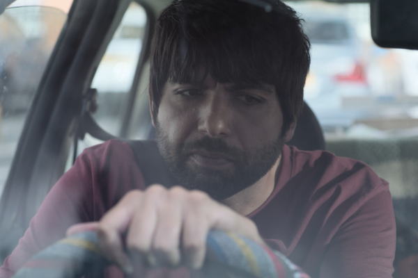 Man sits behind wheel of car looking confused.